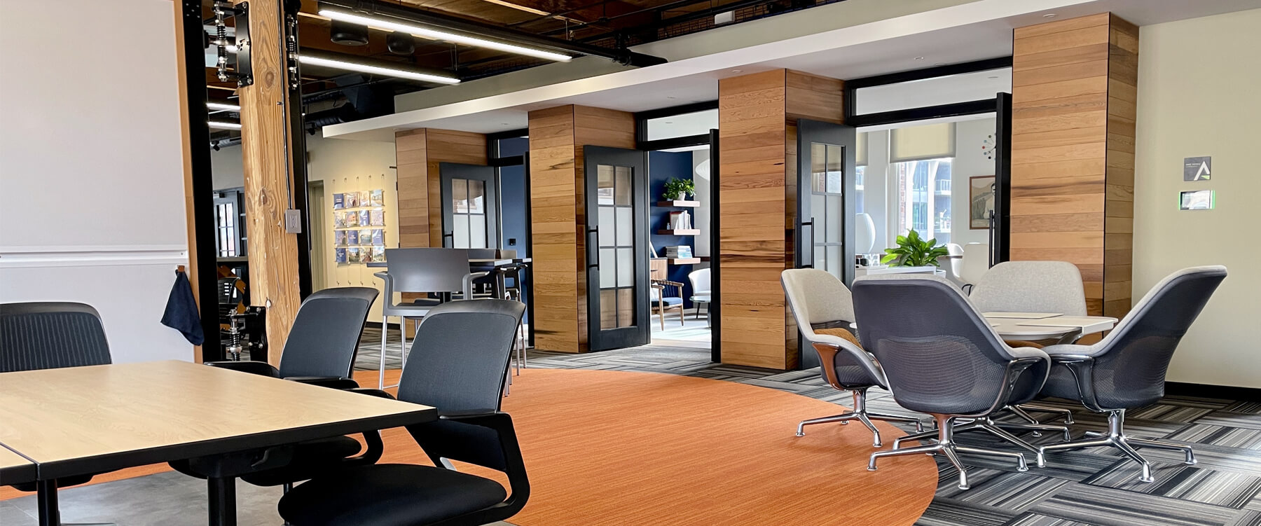 office setting with work tables and office chairs, orange carpet and wall of glass doors open to offices