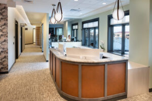 Reception area featuring a curved desk, hanging lights and a hallway to exam rooms and the restroom