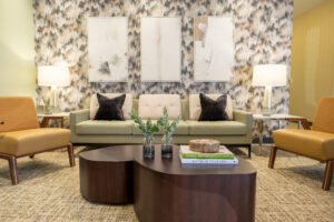 Modern waiting area with wood coffee tables in front of a light green couch with a yellow chair on either side