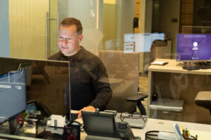 Man working in a shared work space that has multiple desks and computers.