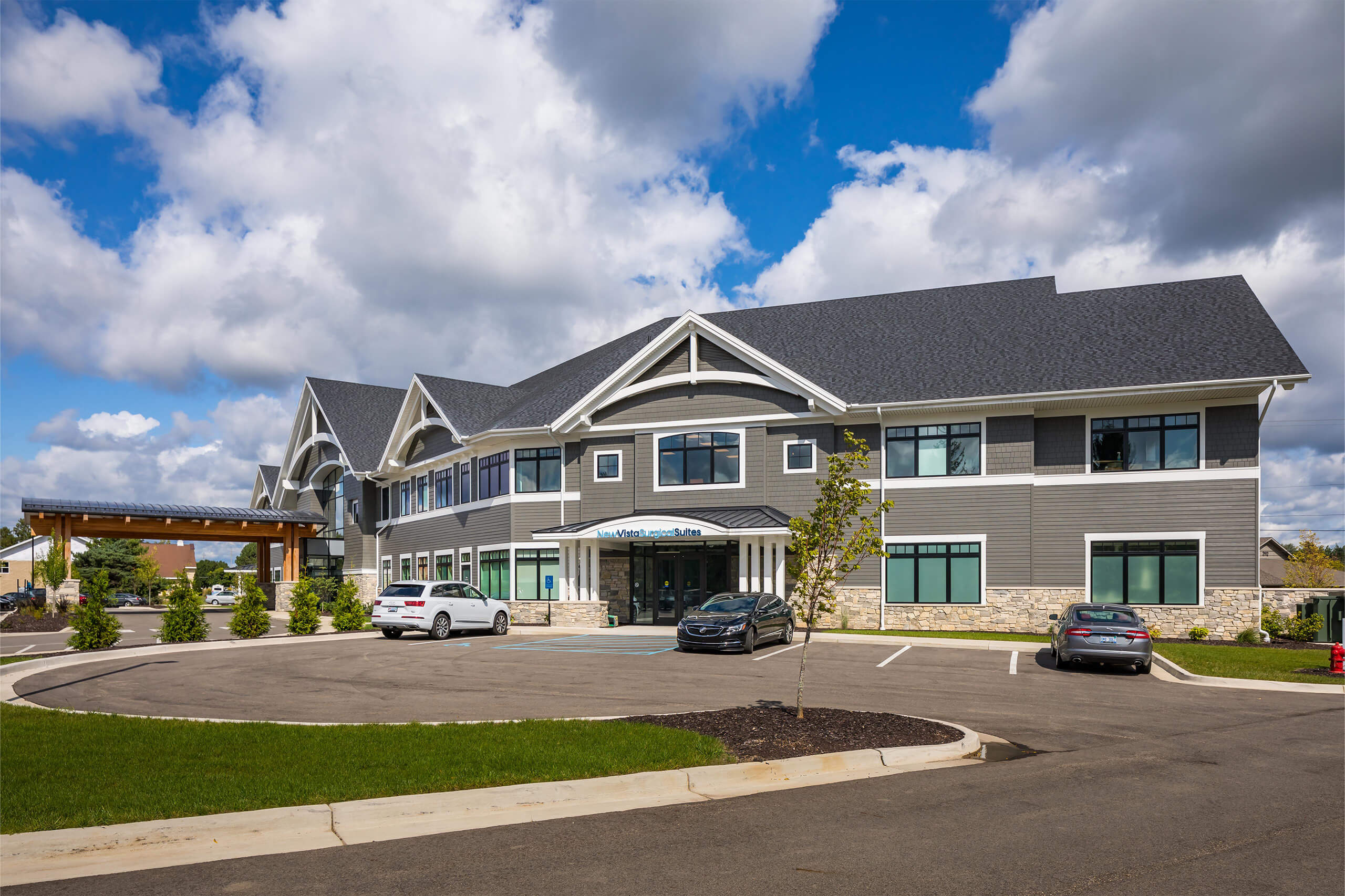 Outdoor view of a gray two-story building with three vehicles parked in front of it in the parking lot