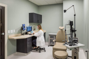 A medical professional in a white coat sitting at a computer in an examining room