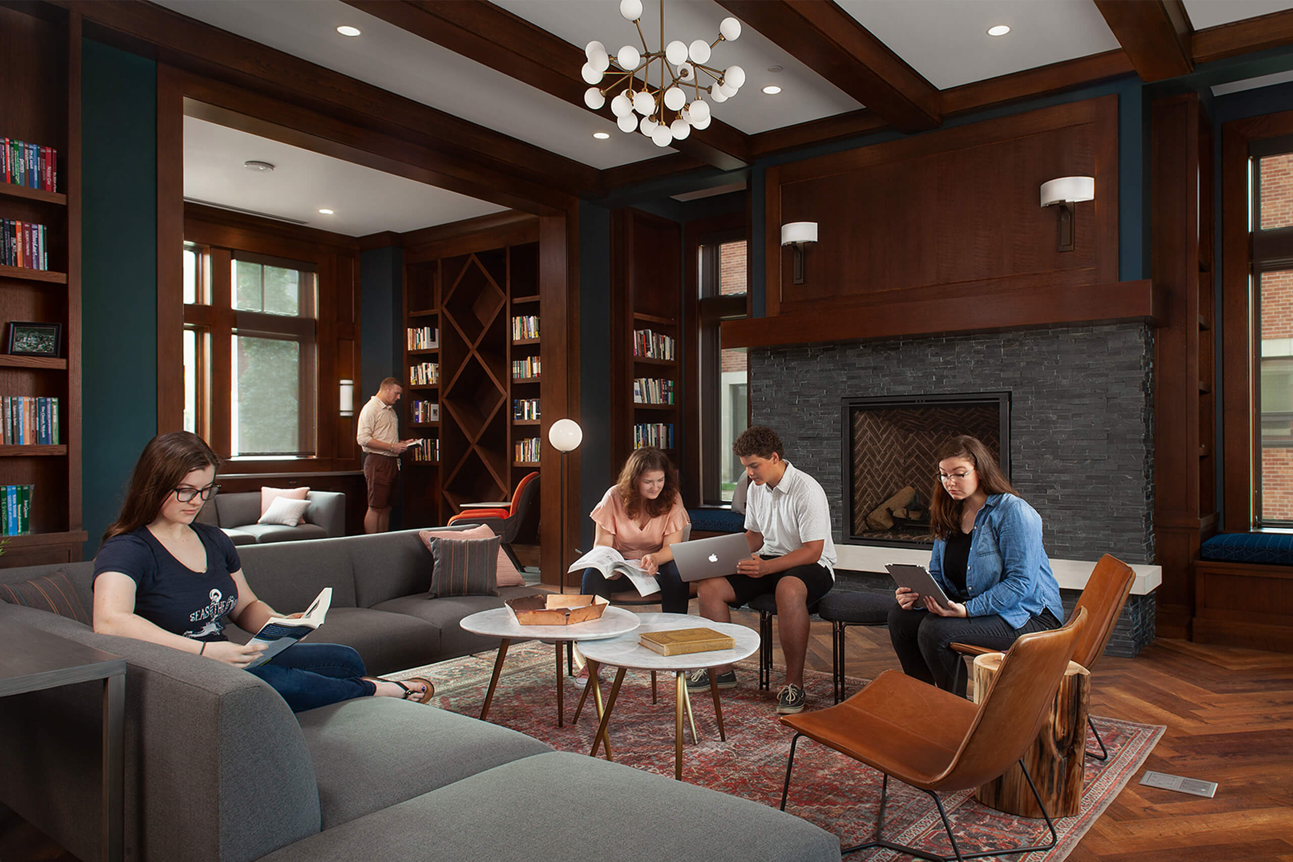 Four students working or reading in various seating options and one student standing next to a bookcase at Hope College Campus Ministries House