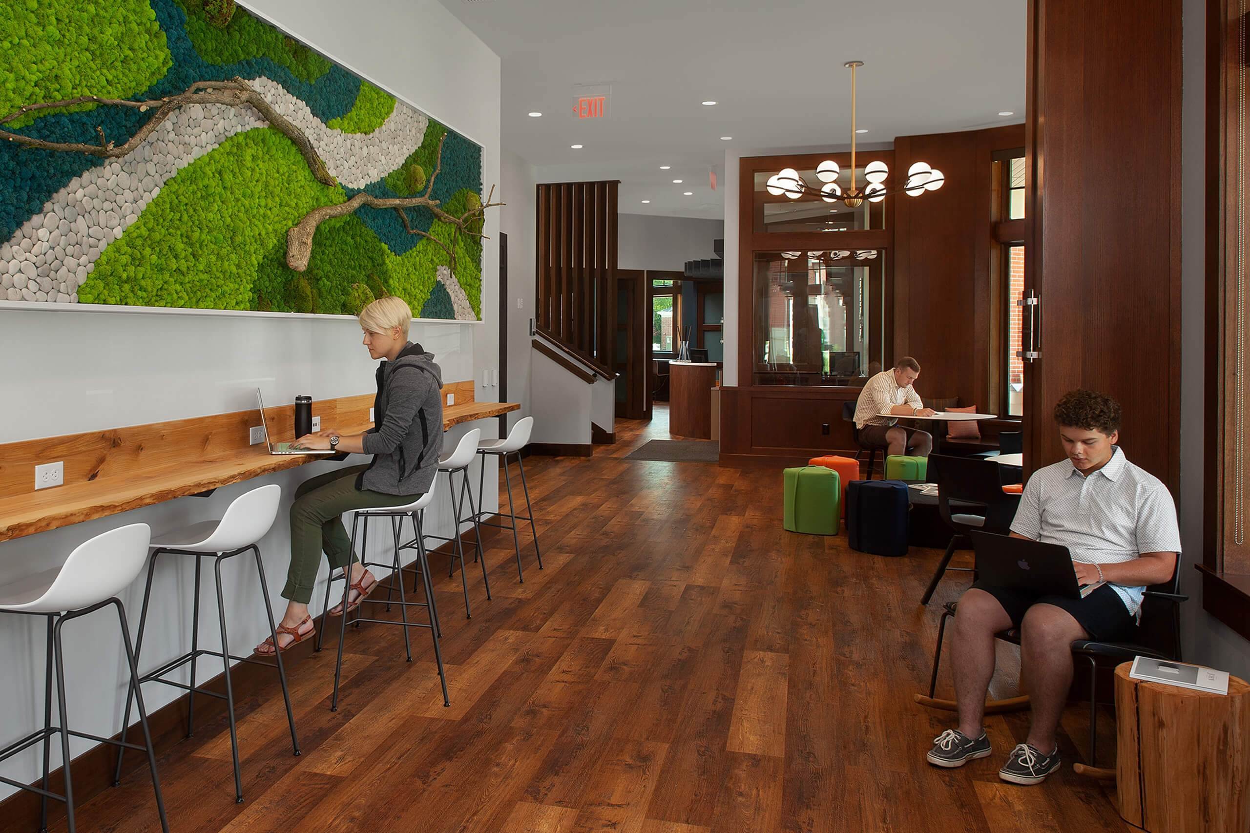 Three students working in the Hope College Campus Ministries House, one seated at a counter top beneath a 3D art piece, one seated in a rocking chair and one seated at a table.