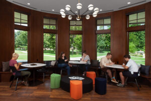 Five students seated at three tables situated in front of large windows