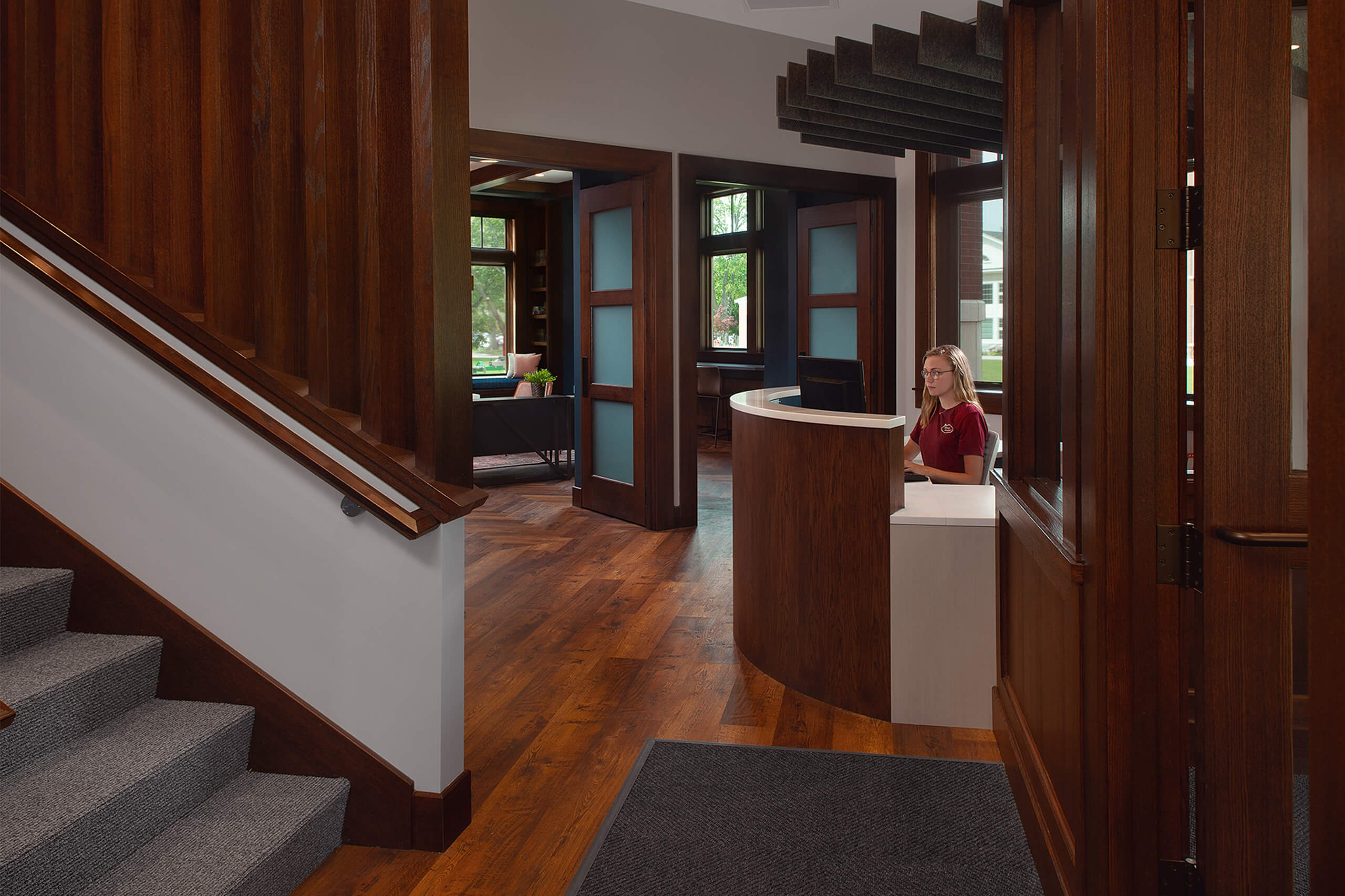 Entry way to the Hope cCollege Campus Ministries House, featuring dark wood accents on the reception desk and doors leading to a lounge area.