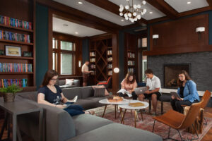 Four students working or reading in various seating options and one student standing next to a bookcase at Hope College Campus Ministries House