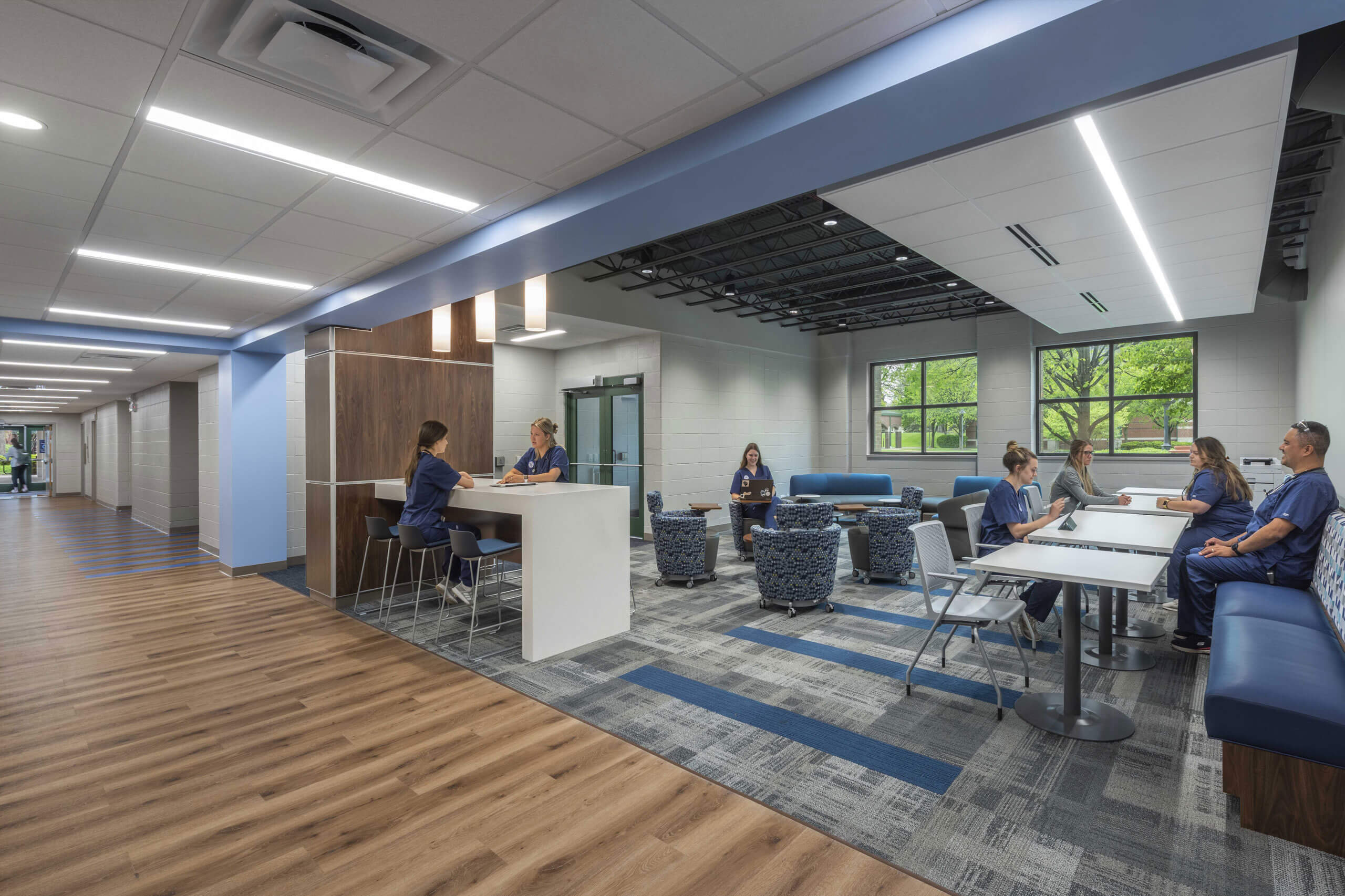 rendering of a nursing facility with a lounge area where 7 people are taking a break including tables, chairs, bench seating and soft seating