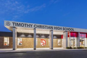 Exterior view of the Timothy Christian High School entrance featuring the logo, large windows and covered walkway