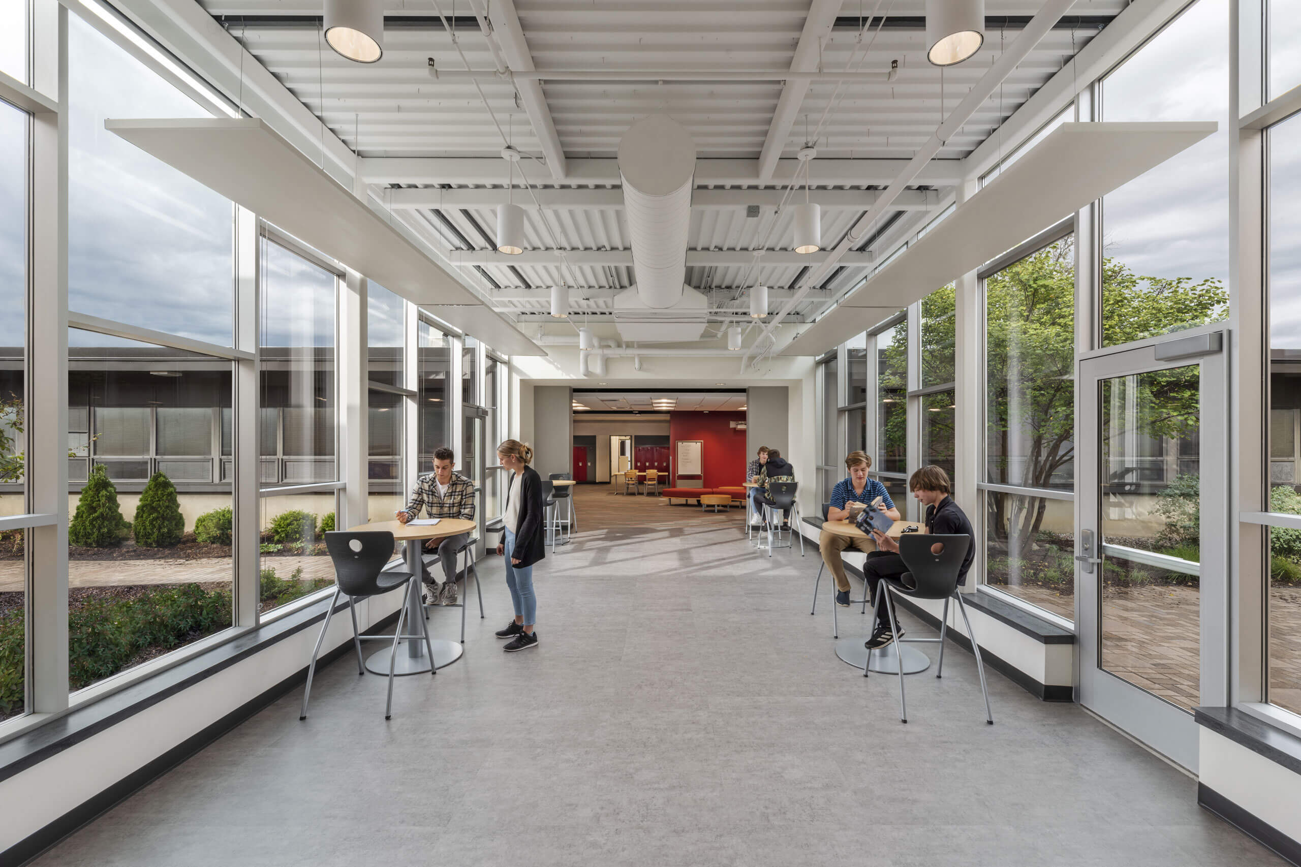 Students sitting at high top tables in a hallway with large windows