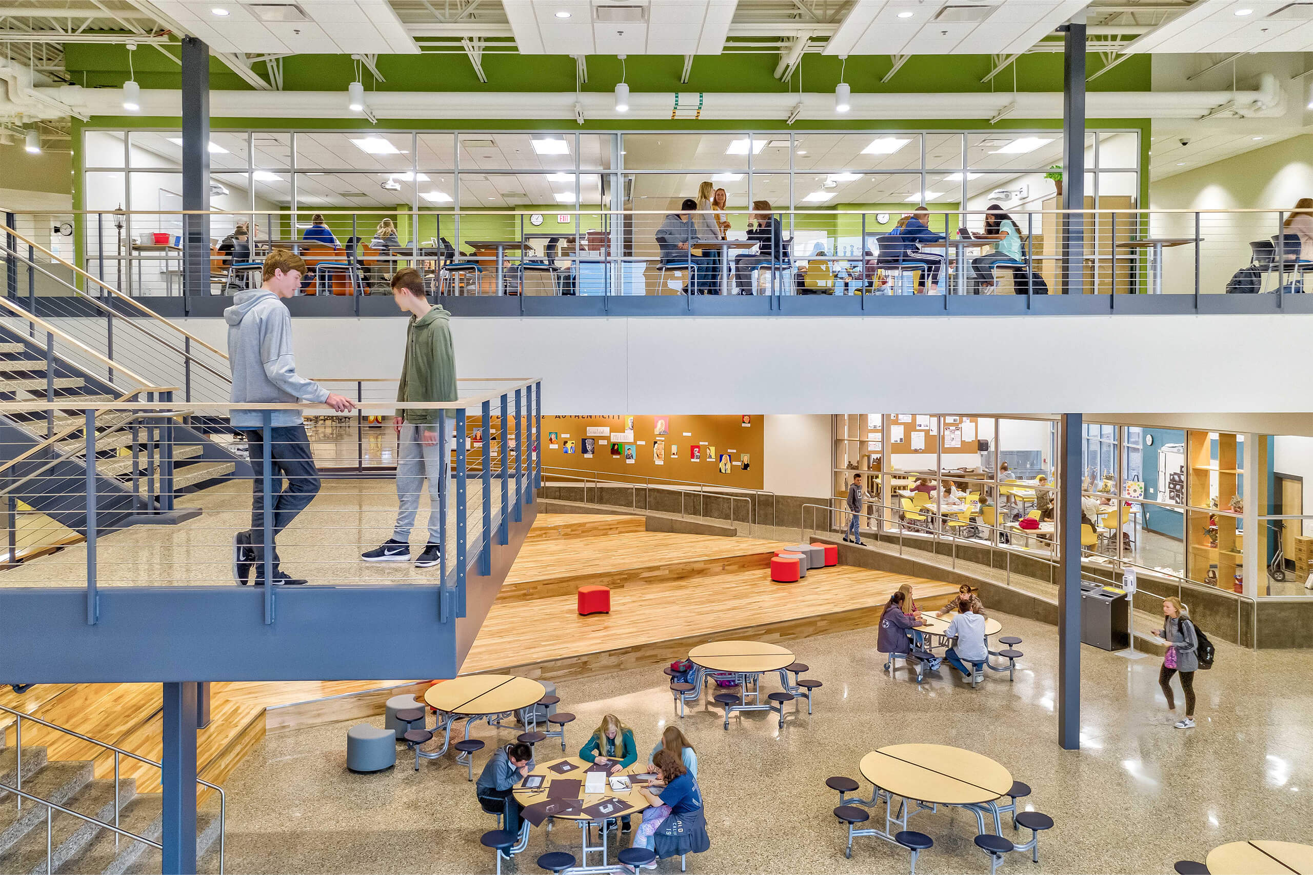 A view of South Christian High School's common spaces that's multiple levels and students are occupying tables and standing on the stairs landing area