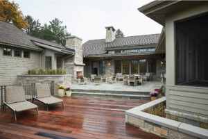 residential family home exterior featuring a wooden deck and stone patio with seating area and stone fireplace