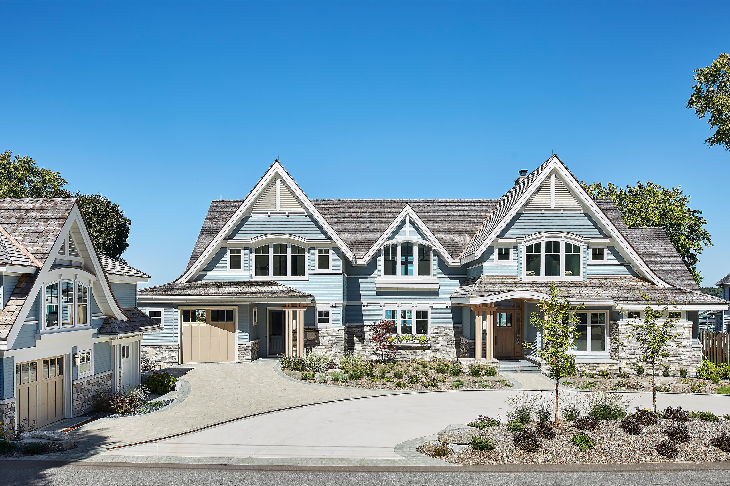 exterior photo of a residential home lakefront cottage with blue siding, white trim, exterior driveway and landscaping