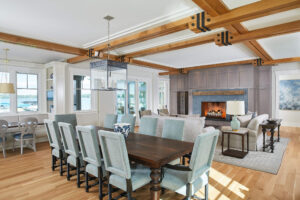 interior view of a residential lakefront cottage focusing on the dining table, couches around the fireplace and view through the windows of the lake