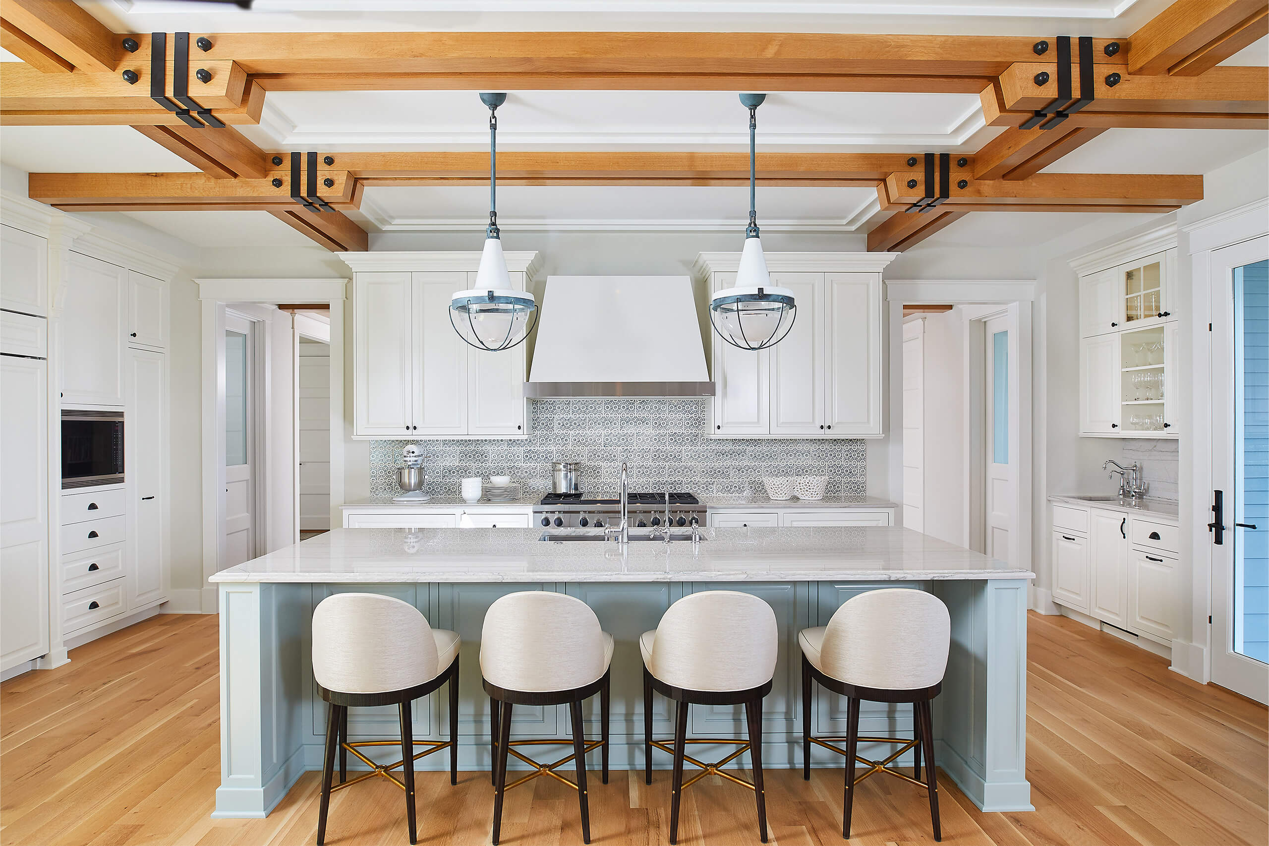 interior view of an open kitchen with barstools over an island with the stove and cabinets behind