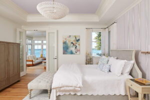 interior view of a white bedroom with french doors open to the seating area behind and lake view through the windows