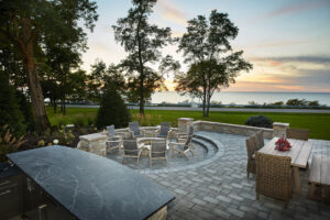 residential home exterior view of a bar area, firepit with chairs and a dining table with chairs looking out over the lake