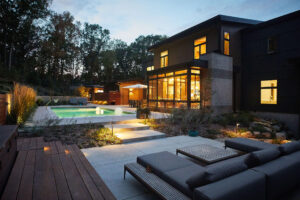 exterior view of a modern residential home lit up from within at dusk featuring the pool and deck area