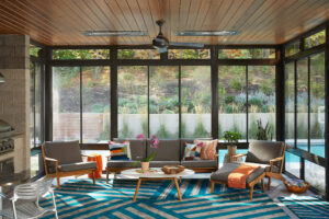 interior view of a poolside room with full glass walls featuring seating area and a grill