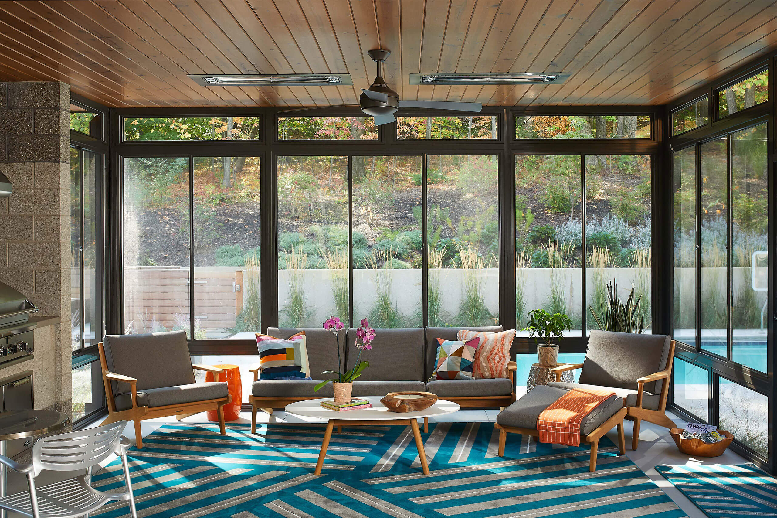 interior view of a poolside room with full glass walls featuring seating area and a grill