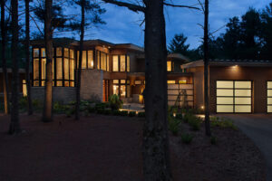 A modern home in the woods at night with the interior lit up through the windows