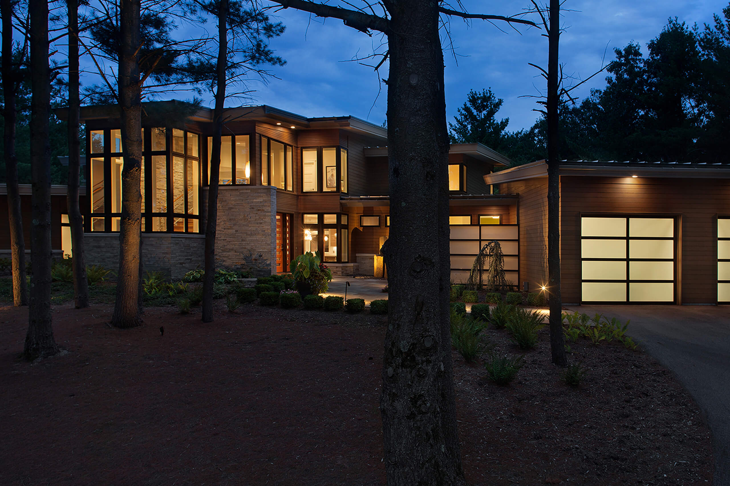 A modern home in the woods at night with the interior lit up through the windows