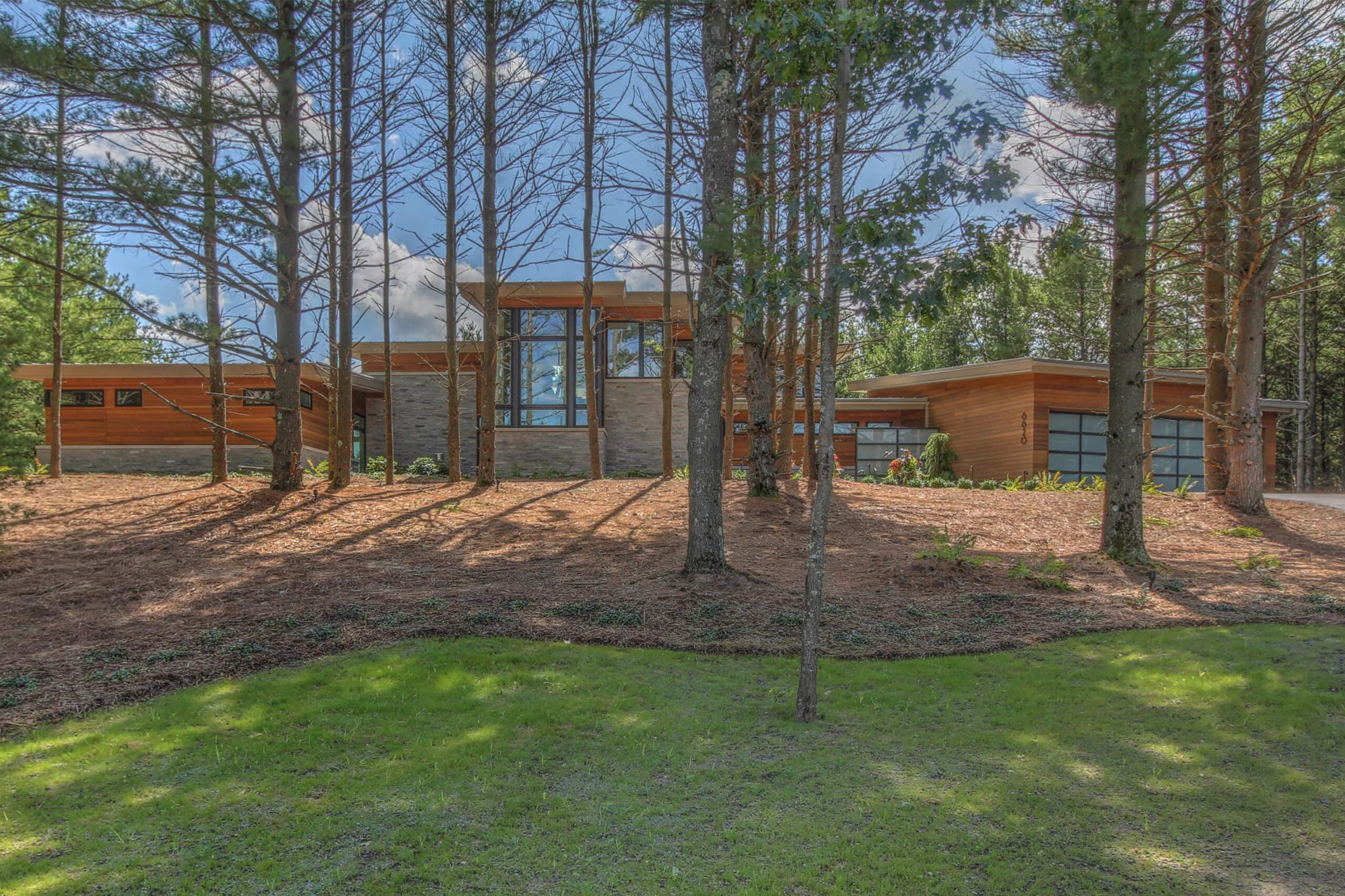 exterior view of a modern residential home looking through pine trees toward the home in daylight featuring exterior facade