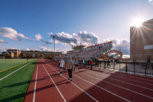 Athletes walking on the track with the bleachers in the background at Trojan Stadium