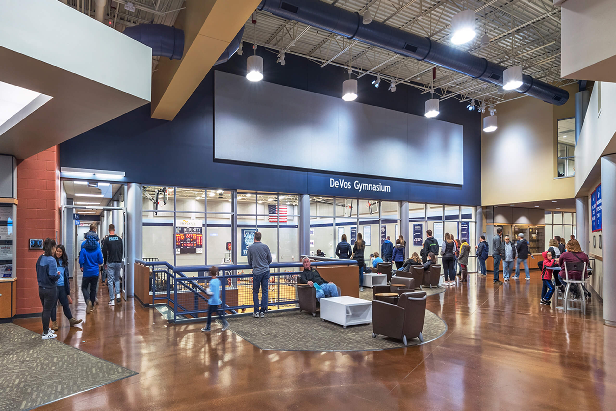 Interior of DeVos Gymnasium with people walking and sitting in a spacious lobby area that overlooks the basketball court