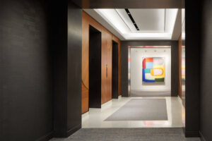 interior view looking down a hallway toward elevators and a modern art piece hanging on the wall