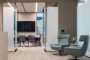 interior view of a modern office workspace with soft chairs in a hallway with glass doors open to a conference room