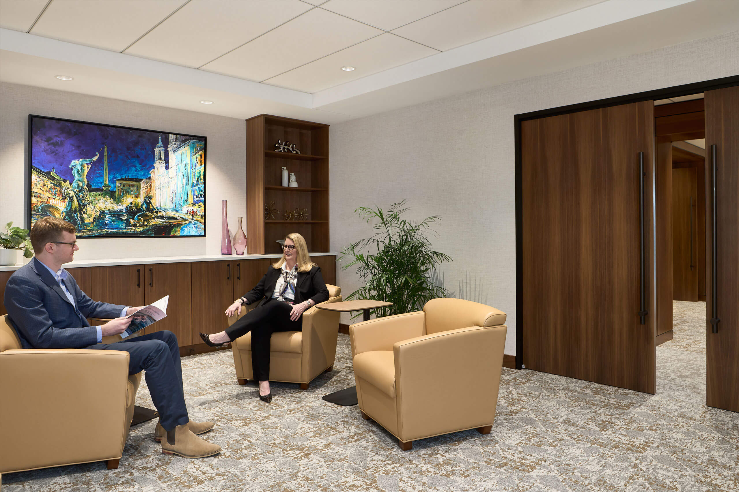 two coworkers sit in yellow chairs talking in an office setting indoors