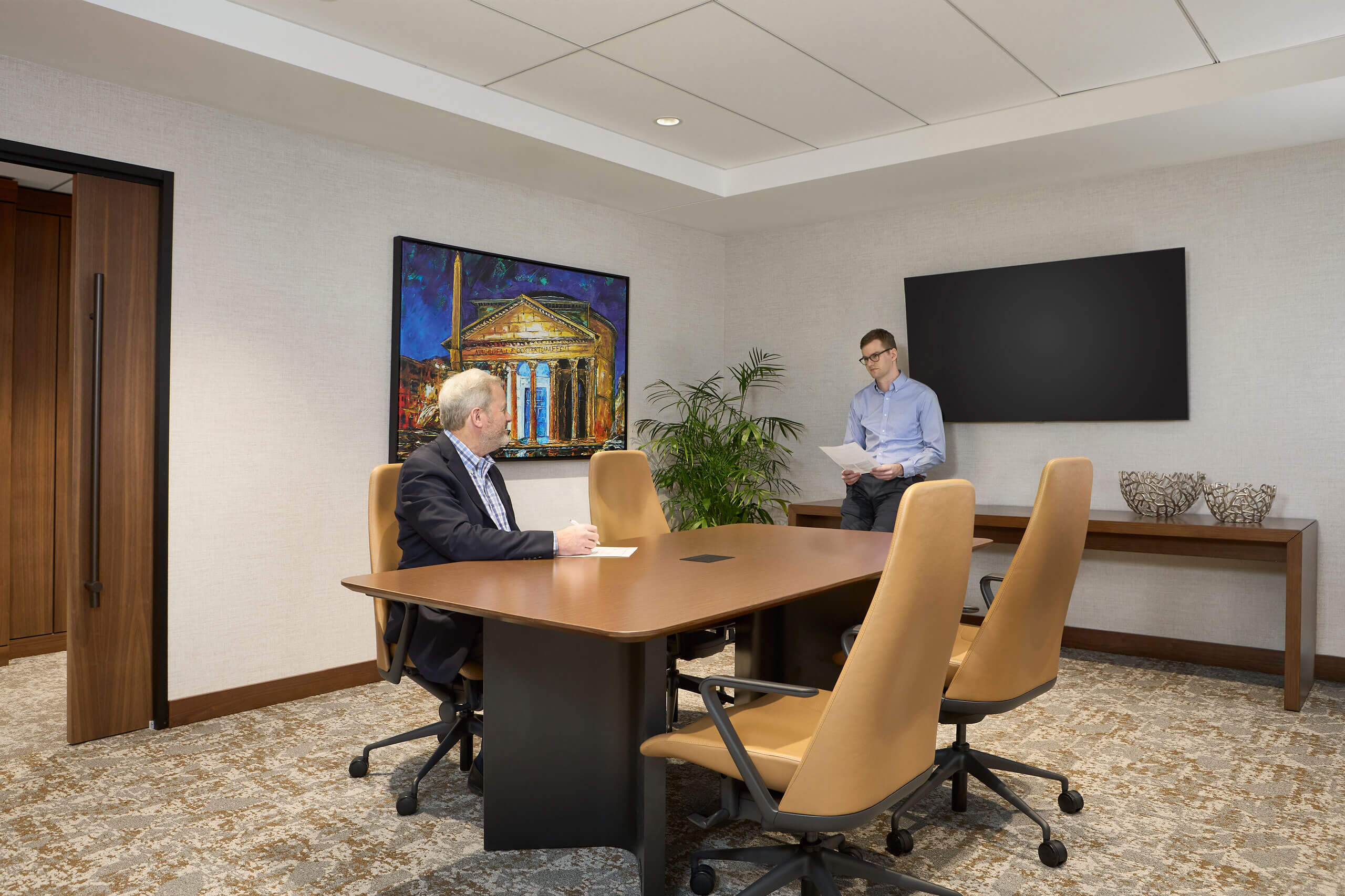 two men talk inside a modernly decorated conference room