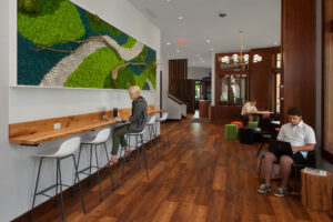 Three students working in the Hope College Campus Ministries House, one seated at a counter top beneath a 3D art piece, one seated in a rocking chair and one seated at a table.