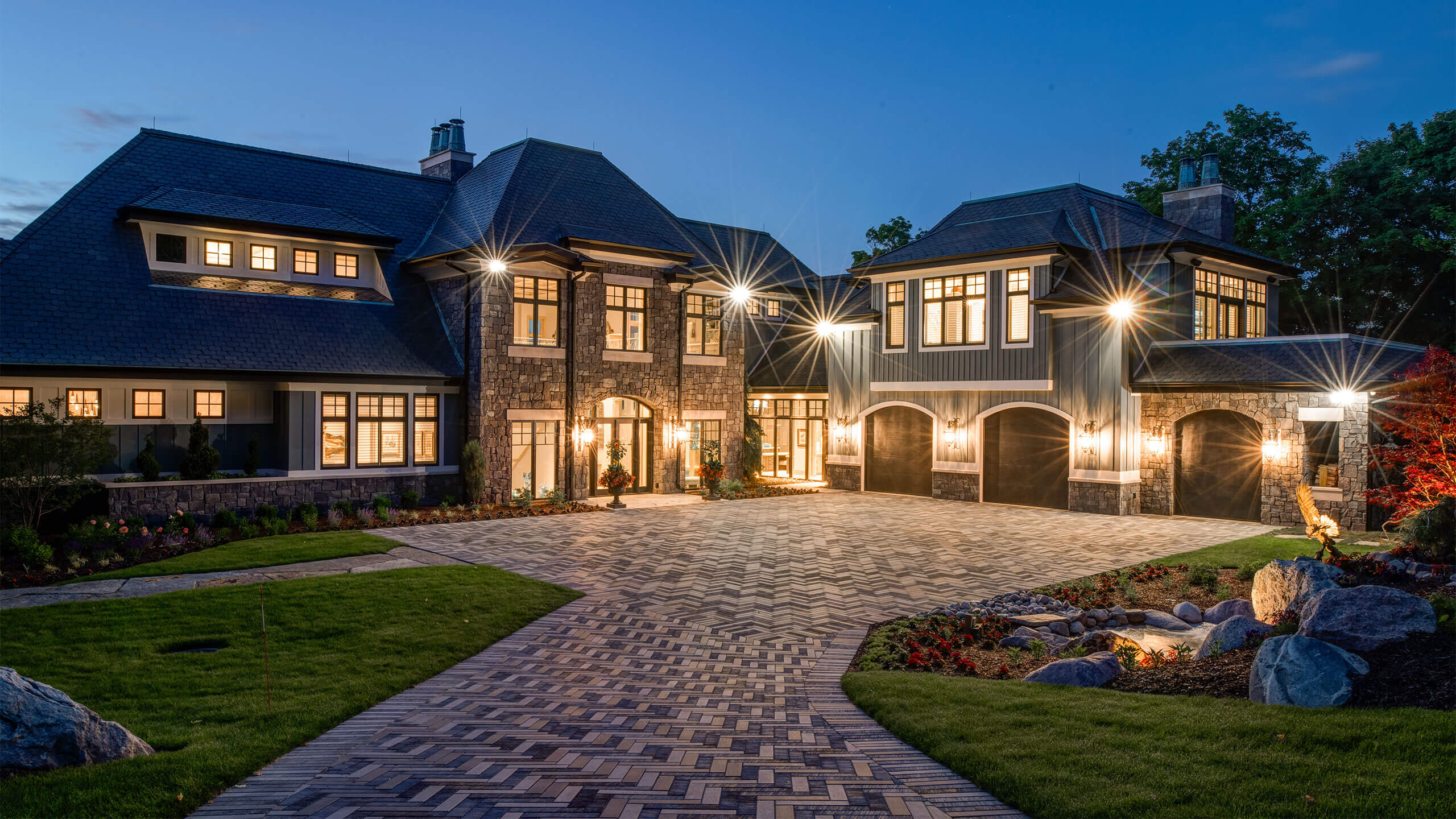 exterior night photo of a large residential home lit from within with a brick inlay driveway