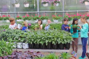 Seven students hold different pots of green plants at the Integrated Outdoor Education building at Ada Christian School