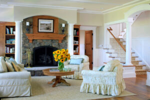 yellow living room with oak flooring, a rock fireplace and oak mantle and skirted chairs and couch