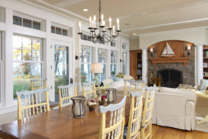 interior of a lake cottage with a dining table, living room area and white windows and doors facing the lake