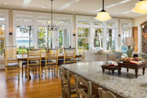 interior of a lake cottage with a dining table, breakfast bar, living room area and white windows and doors facing the lake