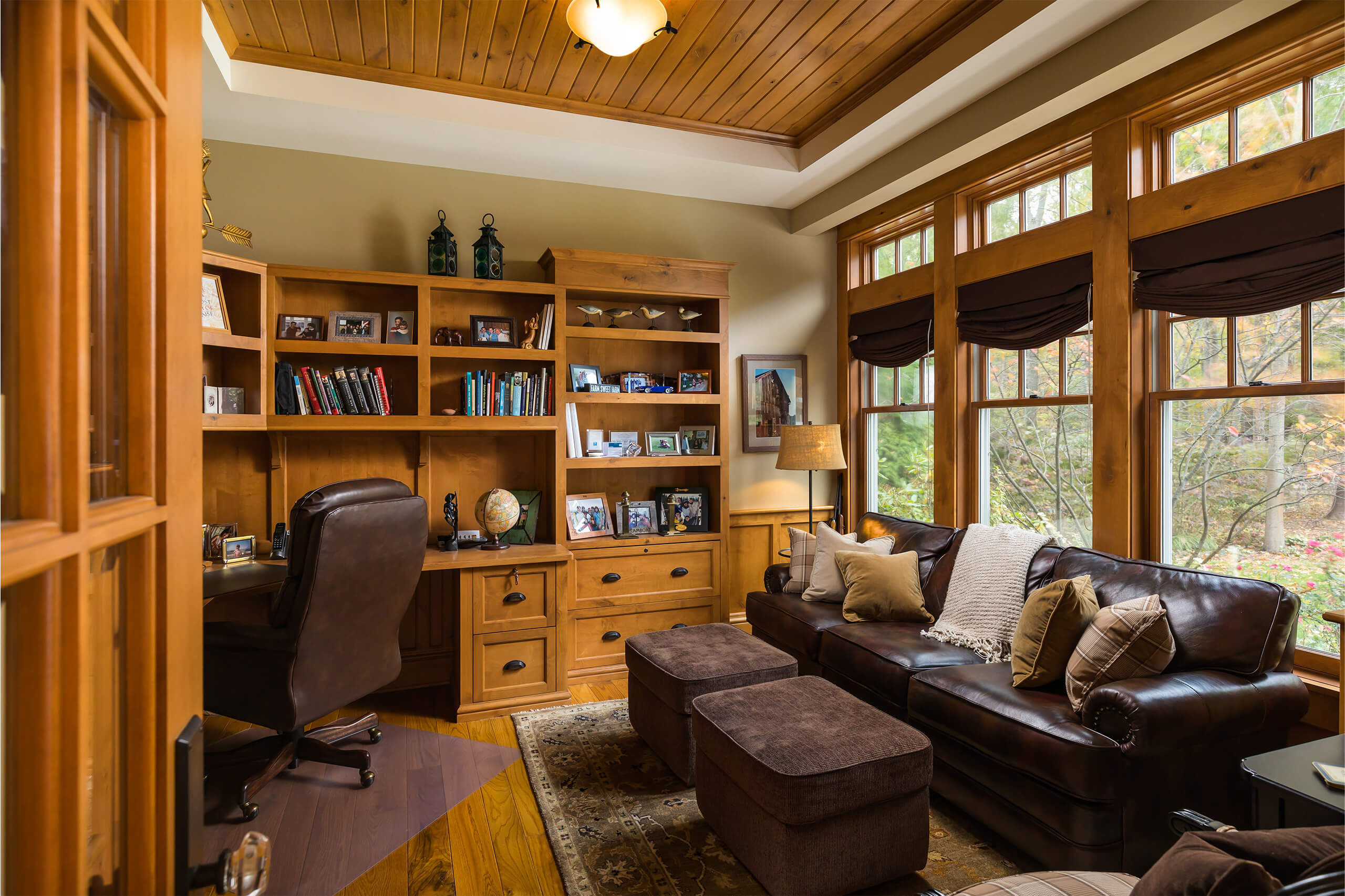 Interior office with oak desk and bookshelfs, oak ceiling, oak window trim, oak flooring and oak door and a brown leather couch