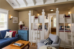 interior room of a shingle-style cottage with two sets of white bunk beds and a seating area