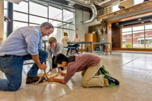 Teacher shows two boys how to make a wooden and string bow at the Integrated Outdoor Education building at Ada Christian School