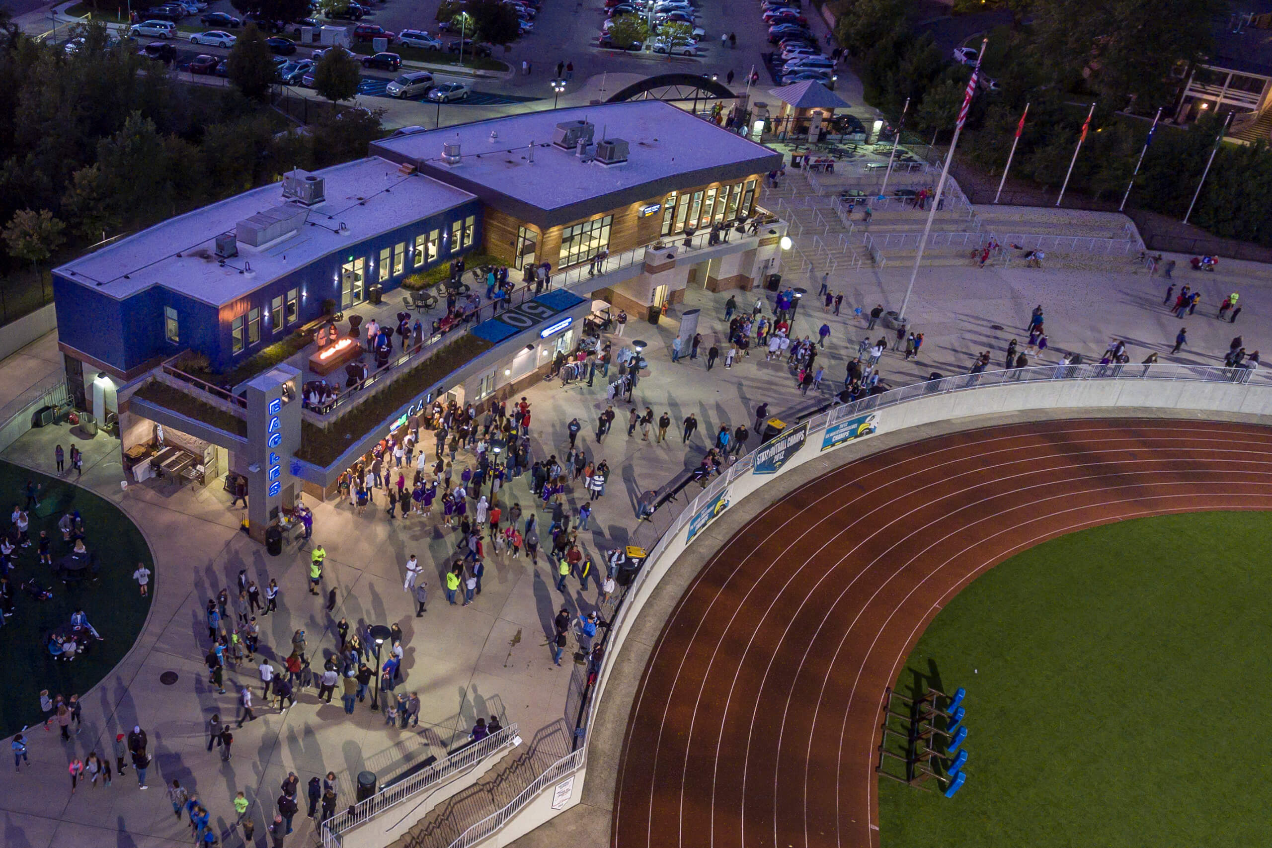 nighttime aerial of plaza full of people and building set at the endzone of a football field