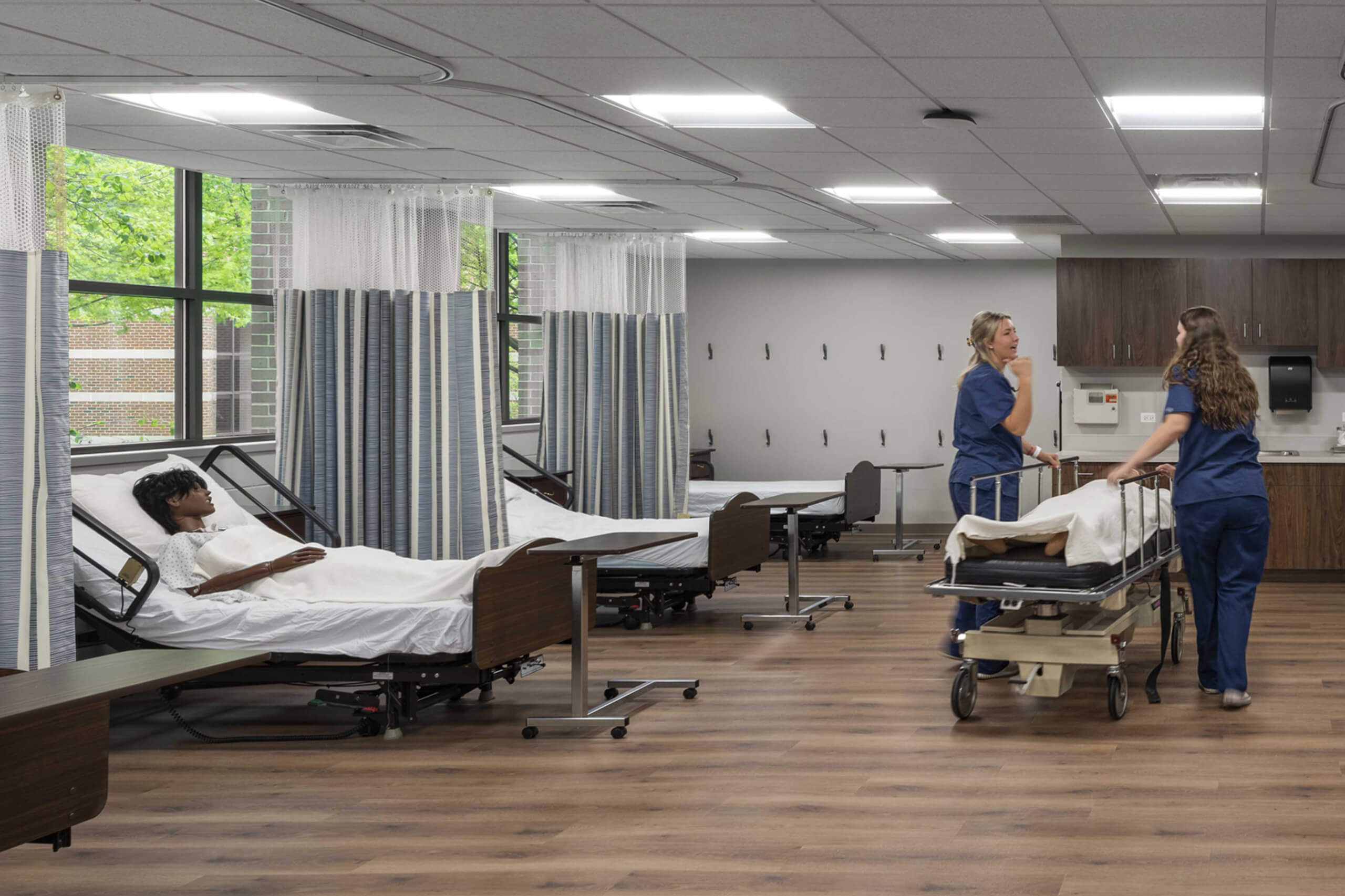 photo of a healthcare room with multiple patient beds and healthcare staff checking on patients