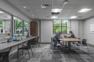 Interior of a gray brick room with gray carpeting, a table with 8 chairs and two people showing an iPad