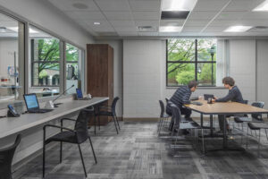 Interior of a gray brick room with gray carpeting, a table with 8 chairs and two people showing an iPad