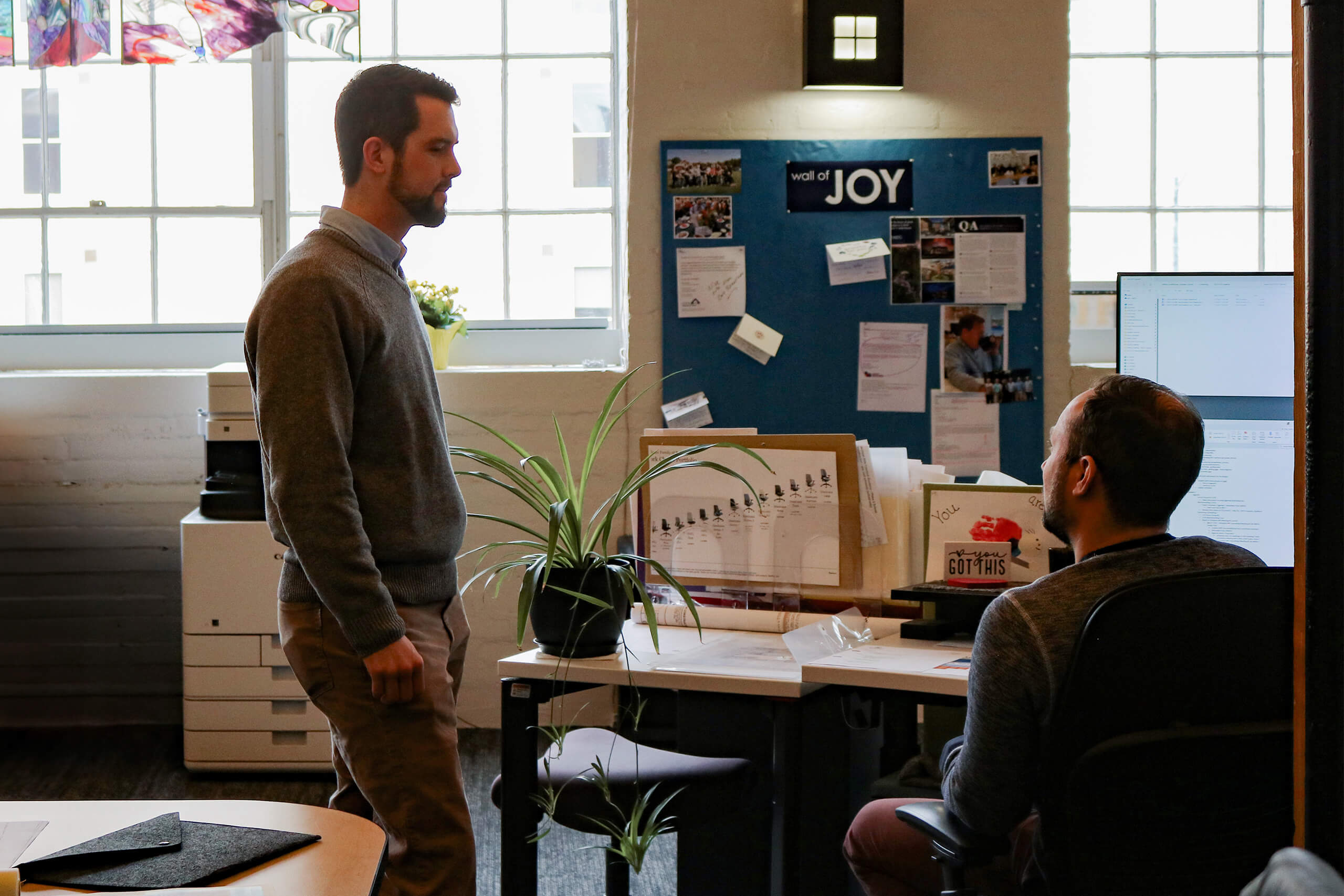 two people talking in front of a window and cork board