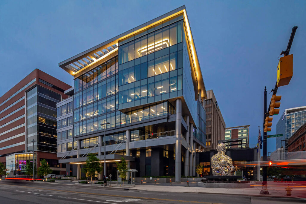 nighttime exterior of a downtown building with glass facade and large sculpture