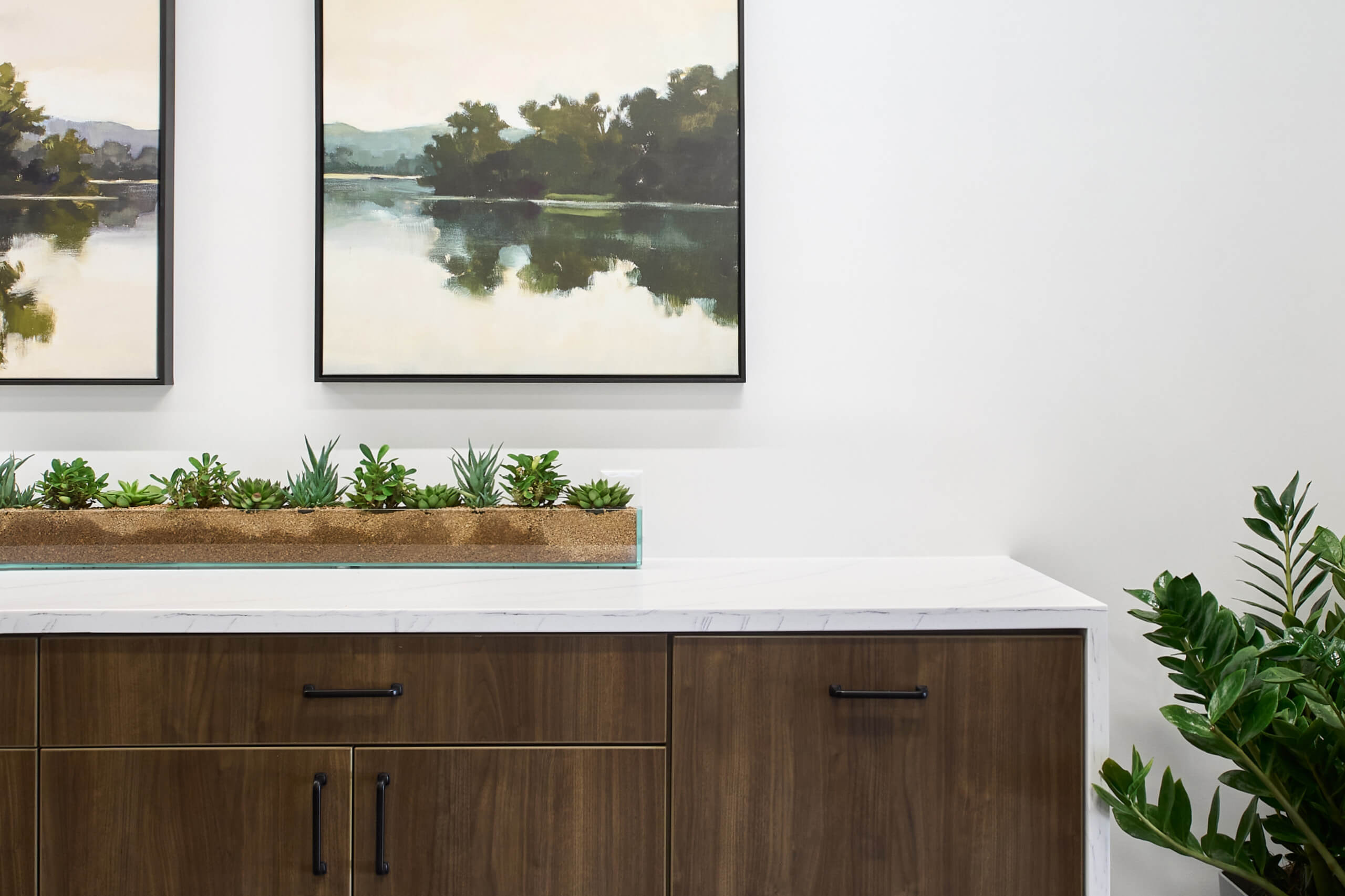 detail of paintings hanging over a waterfall edge counter with wooden drawer and cabinet fronts