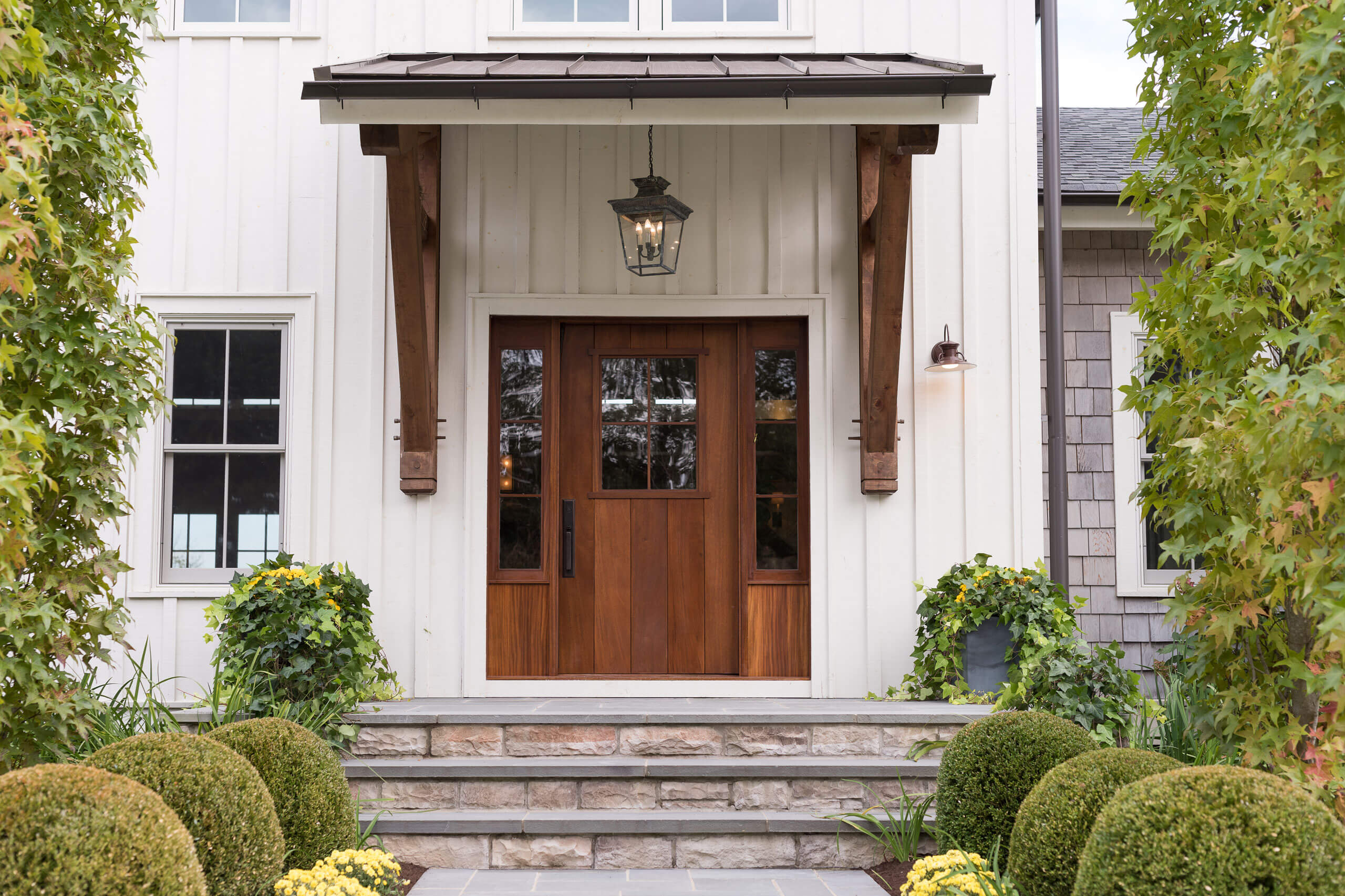 landscape lined residential entry with rich wooden door and metal roof overhang